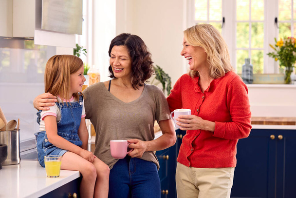 Same Sex Family With Two Mature Mums And Daughter Sitting In Kitchen Talking Together - Foto, Imagen