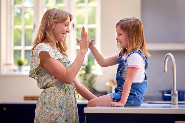 Family At Home With Daughter Sitting On Kitchen Counter Giving Mother High Five - Фото, зображення