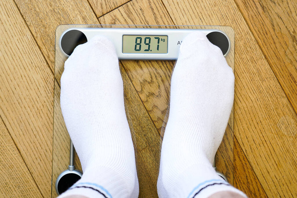 Чоловік у білих шкарпетках важить себе на прозорому електронному підлозі, вага читання 89 кг, вид зверху
 - Фото, зображення