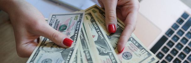 Les mains de femme tenant des billets en dollars gagnés en travaillant à partir d'un ordinateur portable à la maison sur Internet. Télétravail et concept de télétravail - Photo, image