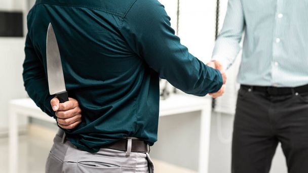 Back view of businessman shaking hands with another businessman while holding a knife behind his back. Concept of back backstabbing in business, backstabbing between colleagues. - Photo, Image