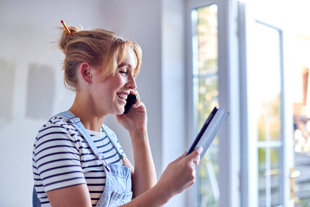 Жінка прикрашає кімнату в будинку роблячи телефонний дзвінок дивлячись на цифровий планшет з фарбою Тестові смуги
 - Фото, зображення