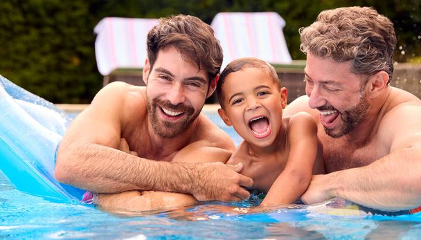 Same Sex Family With Two Dads And Son On Holiday In Swimming Pool Together - Фото, изображение