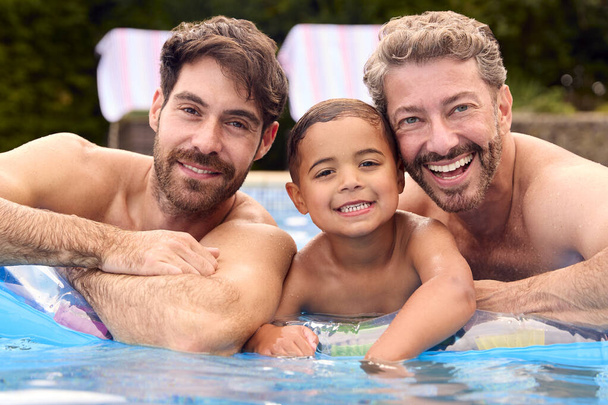 Portrait Of Same Sex Family With Two Dads And Son On Holiday In Swimming Pool Together - Фото, изображение