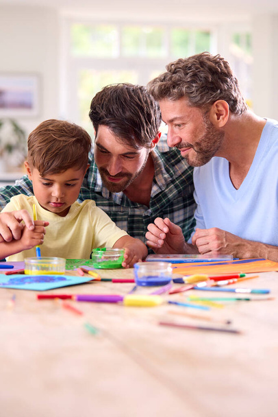 mismo sexo familia con dos papás e hijo pintura cuadro en cocina en casa juntos - Foto, imagen