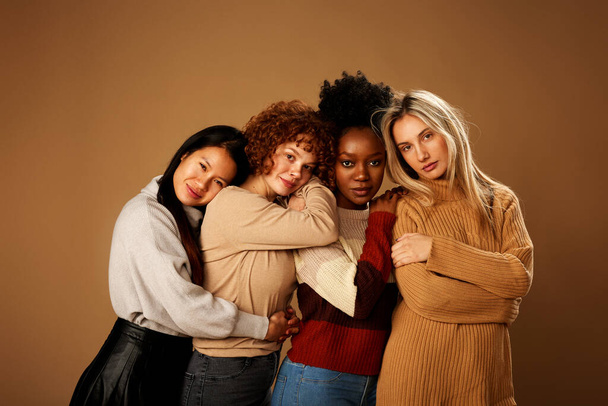 Multicultural girls with pure natural skin posing in studio and looking at the camera isolated on brown background. - Photo, Image