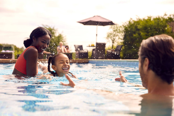 Smiling Mixed Race Family On Summer Holiday Having Fun Splashing In Outdoor Swimming Pool - Фото, изображение
