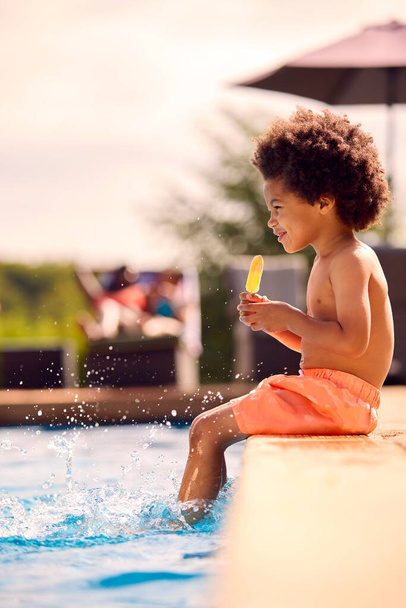 夏休みにはプールの端でアイス・ロリー・スプラッシングを食べる少年と家族 - 写真・画像