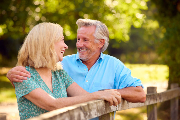 Smiling Casually Dressed Mature Or Senior Couple Leaning On Fence On Walk In Countryside - Foto, Imagem