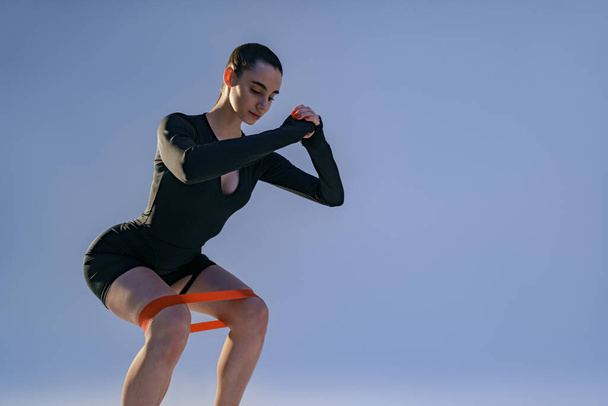 Спортсменка тренує ноги з фітнес-еластичною стрічкою на студійному фоні. Високоякісна фотографія
 - Фото, зображення