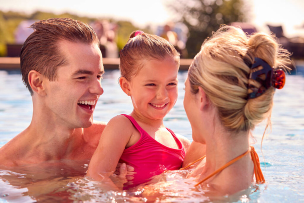 Smiling Family On Summer Holiday Relaxing In Swimming Pool - 写真・画像