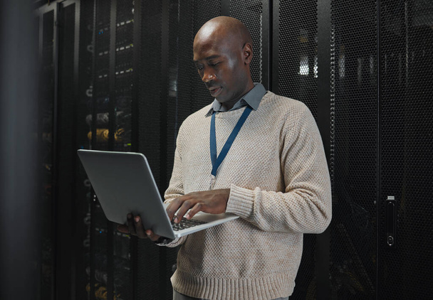 Server room, laptop and black man technician with data center management, system and cybersecurity. Focus, serious and inspection of engineering or programmer person with information technology code. - Fotó, kép