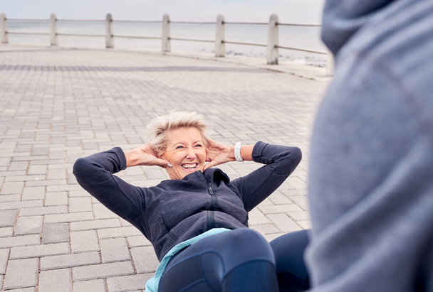 Starsza kobieta, fitness i usiąść z osobistym trenerem na plaży dla silnego treningu brzucha lub ćwiczeń. Zadowolona starsza pani uśmiech dla rdzenia, żołądka lub brzucha szkolenia z trenerem zdrowia nad morzem. - Zdjęcie, obraz