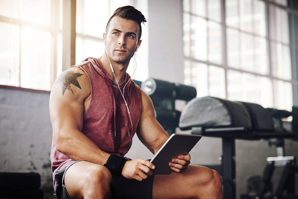 My device is used for music and workout apps. a handsome young man using a tablet at the gym - Photo, Image