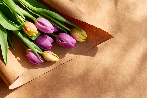 Barevné tulipány na řemeslném papíře.Žluté, růžové, fialové nebo fuchsiové tulipány na hnědém balicím papíru. Tónovaný tón. Jarní dovolená květinový dekor. - Fotografie, Obrázek