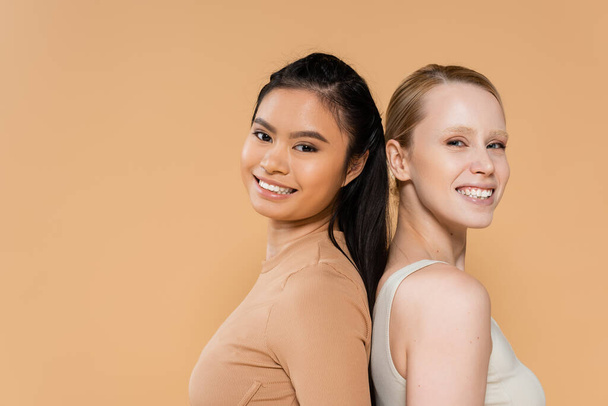 pretty multiethnic women in underwear posing back to back and smiling at camera isolated on beige - Photo, Image