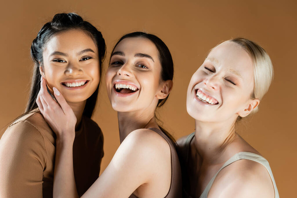 giovani e felici donne multiculturali in biancheria intima sorridenti alla fotocamera isolata sul beige - Foto, immagini
