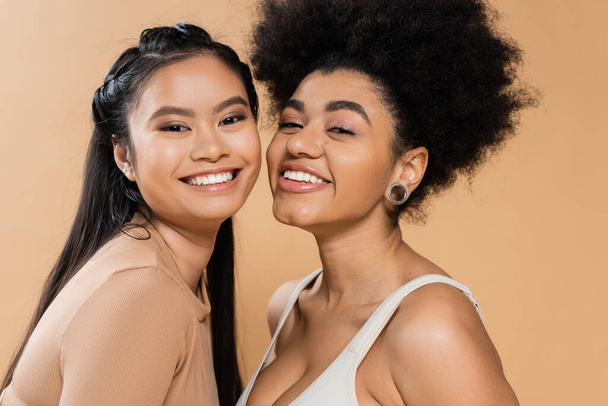 portrait of pretty african american and asian women looking at camera isolated on beige - Foto, imagen