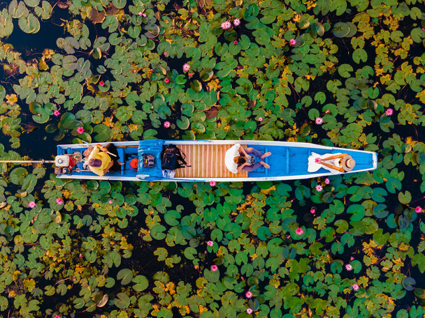 Ζευγάρι σε μια ξύλινη βάρκα στο όμορφο κόκκινο Lotus Θάλασσα Kumphawapi είναι γεμάτη από ροζ λουλούδια στο Udon Thani στη βόρεια Ταϊλάνδη. Χλωρίδα της Νοτιοανατολικής Ασίας.  - Φωτογραφία, εικόνα