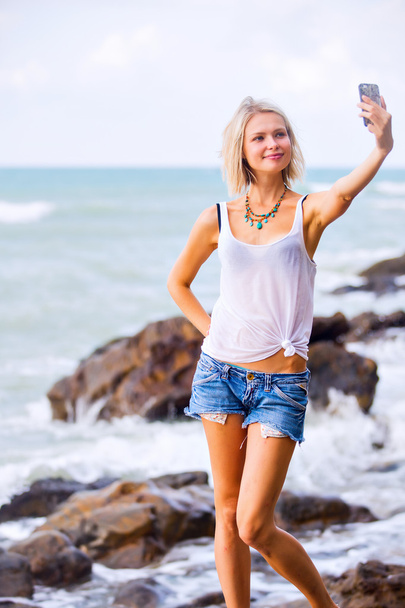 Nő vesz egy selfie, a tenger sziklás partján. - Fotó, kép