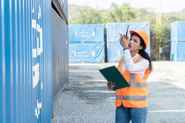 Smiling portrait of beautiful asian female industrial engineer wearing white helmet, vest holding walkie talkie. Safety Supervisor at Container Terminal - Foto, Bild