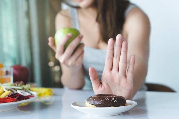 Woman on dieting for good health concept. Close up female using hand push out her favourite donut and choose green apple and vegetables for good health. - Fotografie, Obrázek