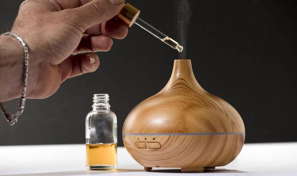 wooden air freshener with steam of natural essences, man's hand with dispenser, blue background - Foto, immagini
