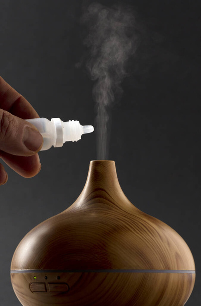 wooden air freshener with steam of natural essences, man's hand with dispenser, black background - Foto, immagini