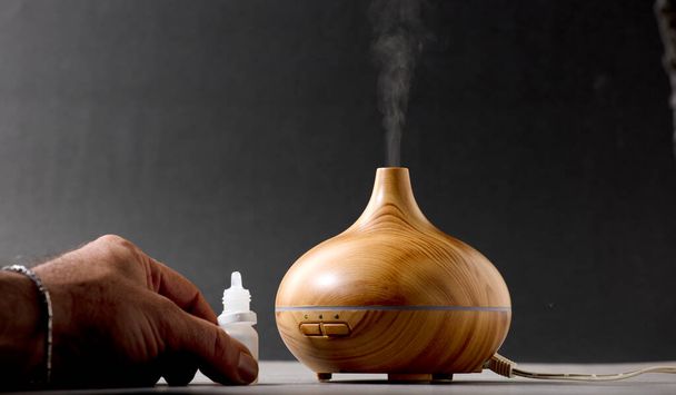 ambientador de madera con vapor de esencias naturales, mano del hombre con dispensador, fondo gris - Foto, imagen