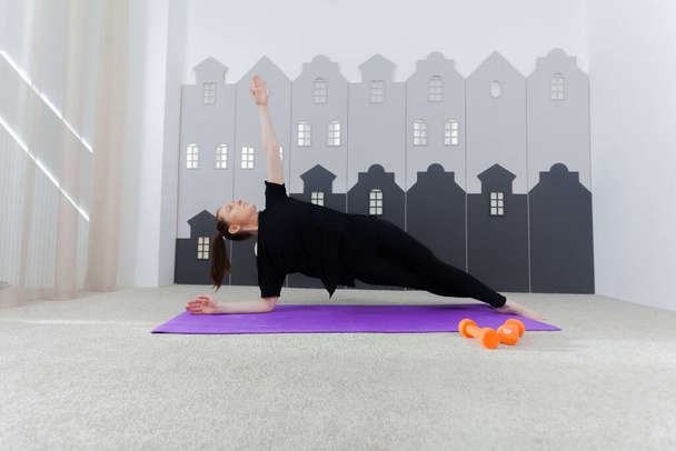 Young attractive woman practicing yoga, working out, wearing sportswear, black top and pants, indoor full length, studio background. Sport and healthy active lifestyle concept. - 写真・画像