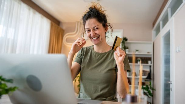 One woman adult caucasian female sit at home happy smile at laptop computer hold bank credit card online shopping concept real people copy space e-commerce - Foto, Bild