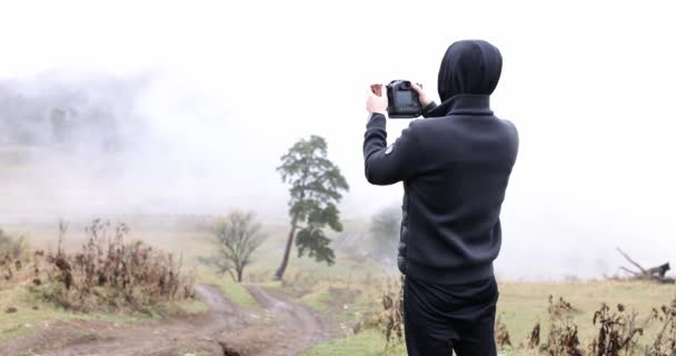 Sylwetka fotografa blogera robiącego zdjęcia przed mglistymi górami. Podróżnik robi zdjęcia gór i krajobrazu naturalnego - Materiał filmowy, wideo