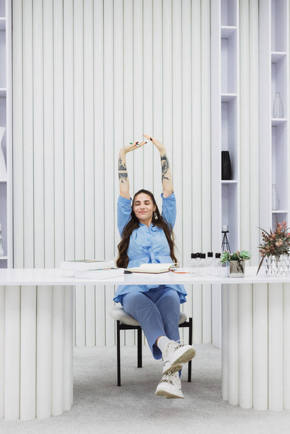 The cosmetic dermatologist takes a brief stretch break while sitting at her desk in this photo. - 写真・画像
