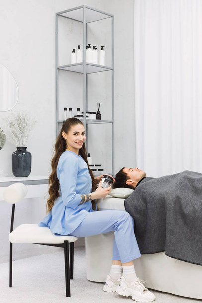 A cosmetic dermatologist works on a patient's skin in a clean, minimalistic white room. The room is bright, tools organized, and the dermatologist's focus reflects her expertise in skin care. - 写真・画像