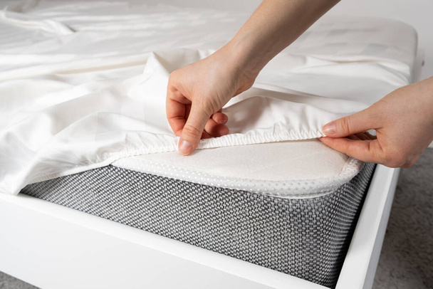 Un drap en satin blanc avec une bande élastique est mis sur le matelas du lit, un gros plan des mains. Linge de lit - Photo, image