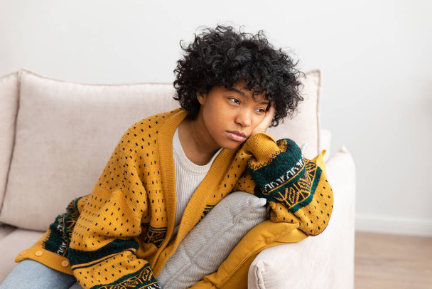 African american sad thoughtful pensive unmotivated girl sitting on sofa at home indoor. Young african woman ponder look tired after long day. Girl feels depressed offended lonely upset heartbreak - Foto, Imagem