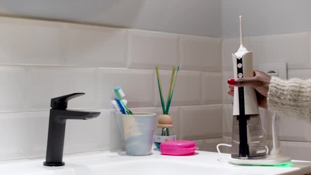 jonge vrouw het nemen en plaatsen van een huishoudelijke draadloze tandheelkundige water flosser op de badkamer wastafel - Video