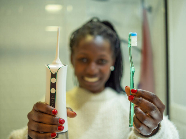 Maintaining a healthy smile: a young woman performs her dental hygiene routine at home using a domestic dental water flosser and her dental toothbrush. - Foto, immagini