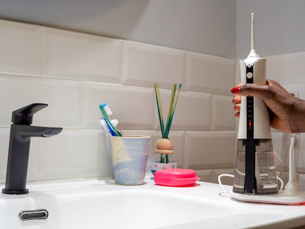 молодая женщина с беспроводной зубной нитью на раковине в ванной комнате - Фото, изображение