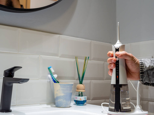  Genç bir adam banyo lavabosunun üzerinde diş ipi tutan bir kablosuz diş ipi tutuyor. - Fotoğraf, Görsel
