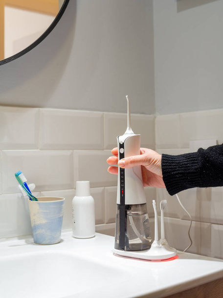 mujer joven sosteniendo un hilo dental inalámbrico doméstico en el lavabo del baño - Foto, Imagen