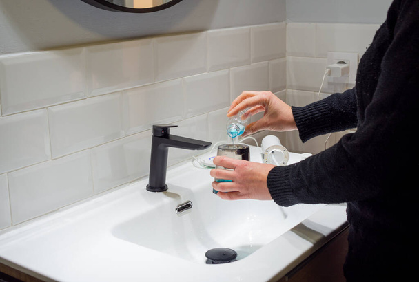Effortless Oral Health: Woman Filling Water Flosser Tank with Mouthwash at Bathroom Basin - Fotó, kép