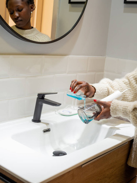Effortless Oral Health: Woman Filling Water Flosser Tank with Mouthwash at Bathroom Basin - Фото, изображение