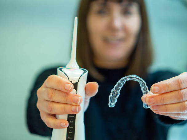Maintaining a healthy smile: a young woman performs her dental hygiene routine at home using a domestic dental water flosser and her dental aligner. - Photo, image