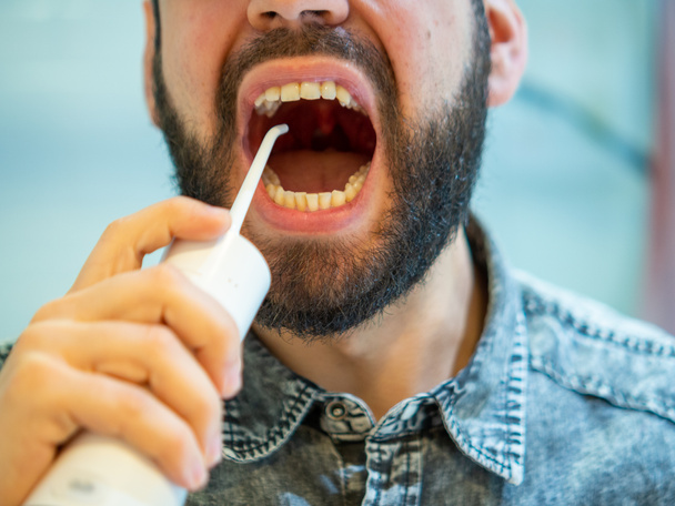 Igiene orale sana: Giovane uomo che utilizza flosser acqua dentale domestica - Foto, immagini