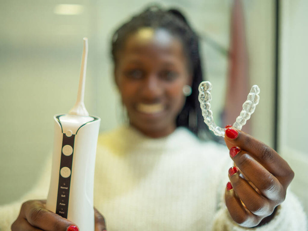 Maintaining a healthy smile: a young woman performs her dental hygiene routine at home using a domestic dental water flosser and her dental aligner. - Fotó, kép
