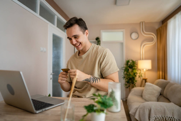 One man adult caucasian male sit at home happy smile at laptop computer hold bank credit card online shopping concept real people copy space e-commerce - Foto, Bild