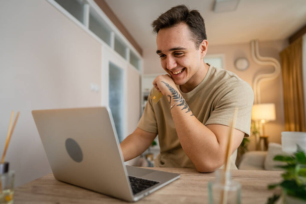 Jeden muž dospělý kavkazský muž sedět doma šťastný úsměv na notebooku držet bankovní kreditní karty on-line nákupní koncept skuteční lidé kopírovat prostor e-commerce - Fotografie, Obrázek