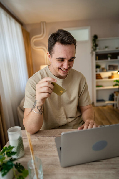 One man adult caucasian male sit at home happy smile at laptop computer hold bank credit card online shopping concept real people copy space e-commerce - Photo, Image