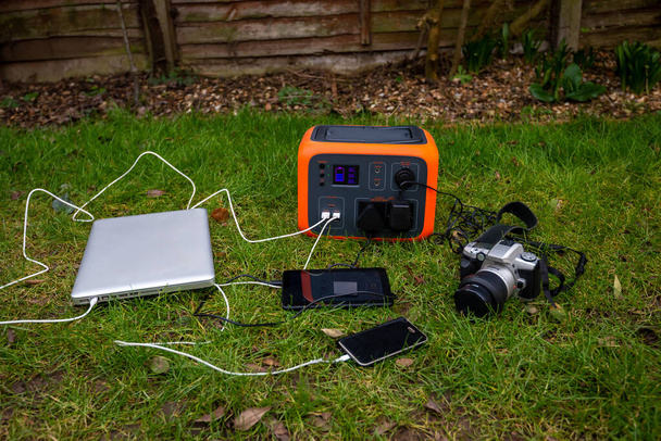 庭の芝生の上で屋外で充電ノートパソコン、タブレットやカメラの電子機器とポータブル発電所太陽光発電。ワイヤレス充電リチウム電池のバックアップどこでも使用可能. - 写真・画像